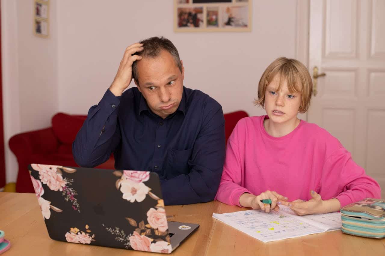 Man and child discussing paperwork at a table, with a laptop displaying floral design, emphasizing the importance of understanding Contract for Deed financing terms.