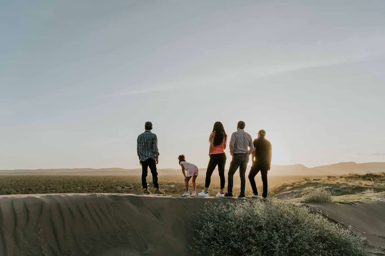 Group of five people standing on a sand dune, overlooking a scenic landscape at sunset, symbolizing community and new beginnings in the context of homeownership and contract for deed agreements in Minnesota.