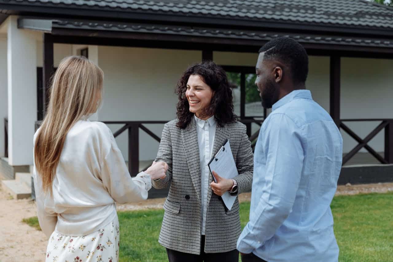 Real estate agent shaking hands with potential homebuyers outside a Minnesota property, discussing Contract for Deed arrangements.