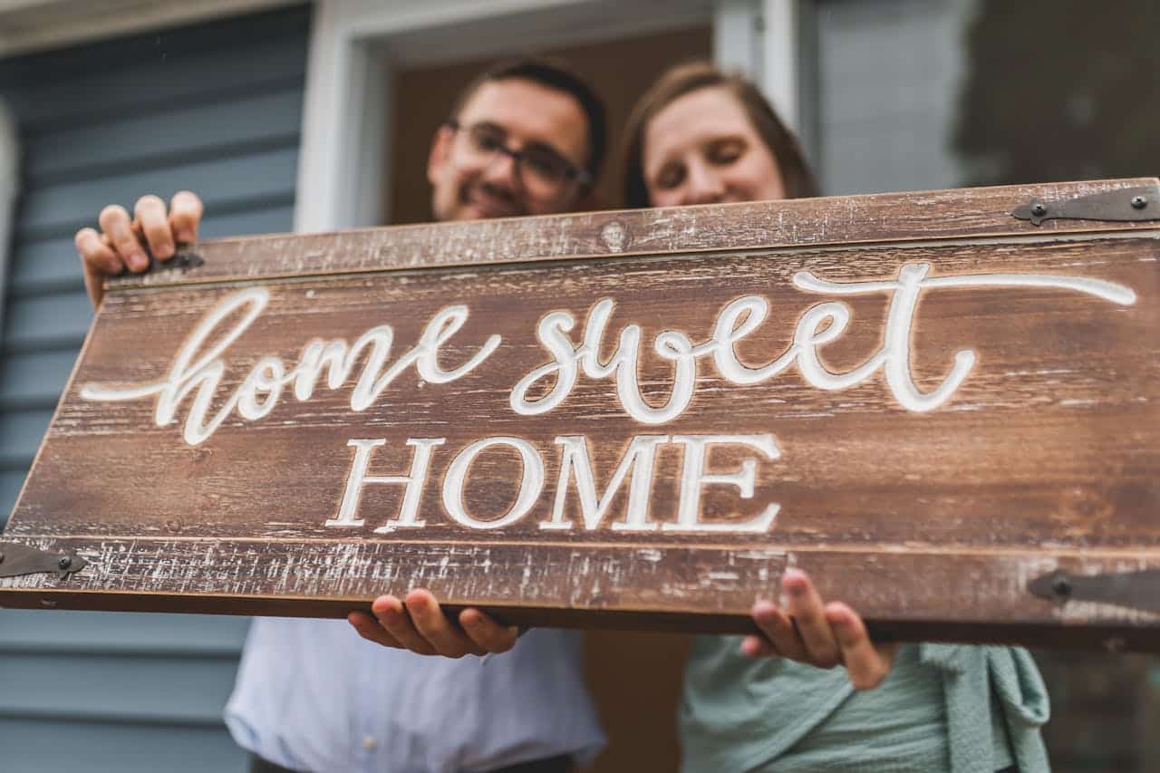 Couple holding a "home sweet home" sign, symbolizing homeownership and the emotional significance of real estate transactions in the context of Contract for Deed agreements.