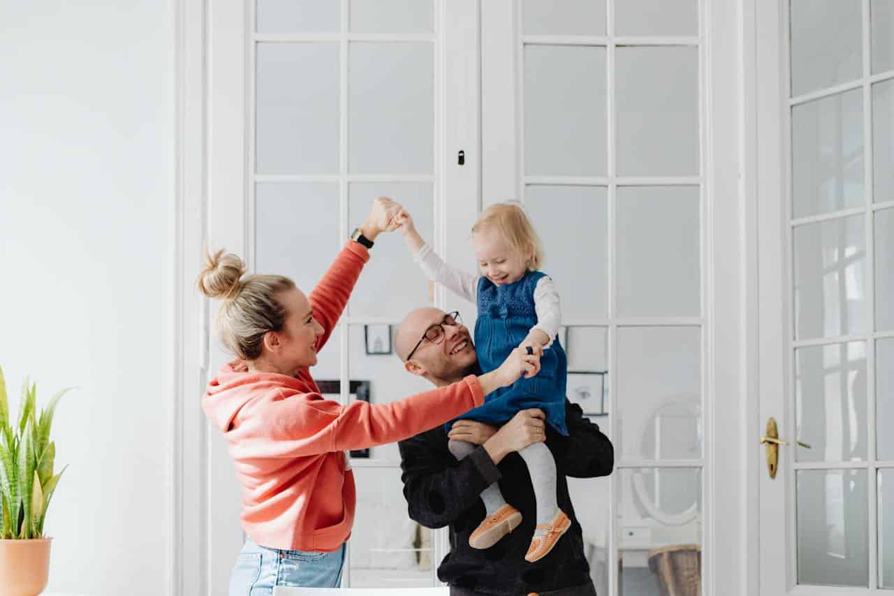 Family celebrating together indoors, with a woman lifting a child while a man holds the child, in a bright, modern living space.