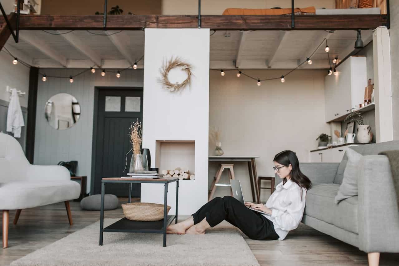 Woman working on a laptop in a modern living room with a cozy atmosphere, featuring a coffee table, decorative elements, and a stylish interior design, reflecting the theme of real estate and land contracts.