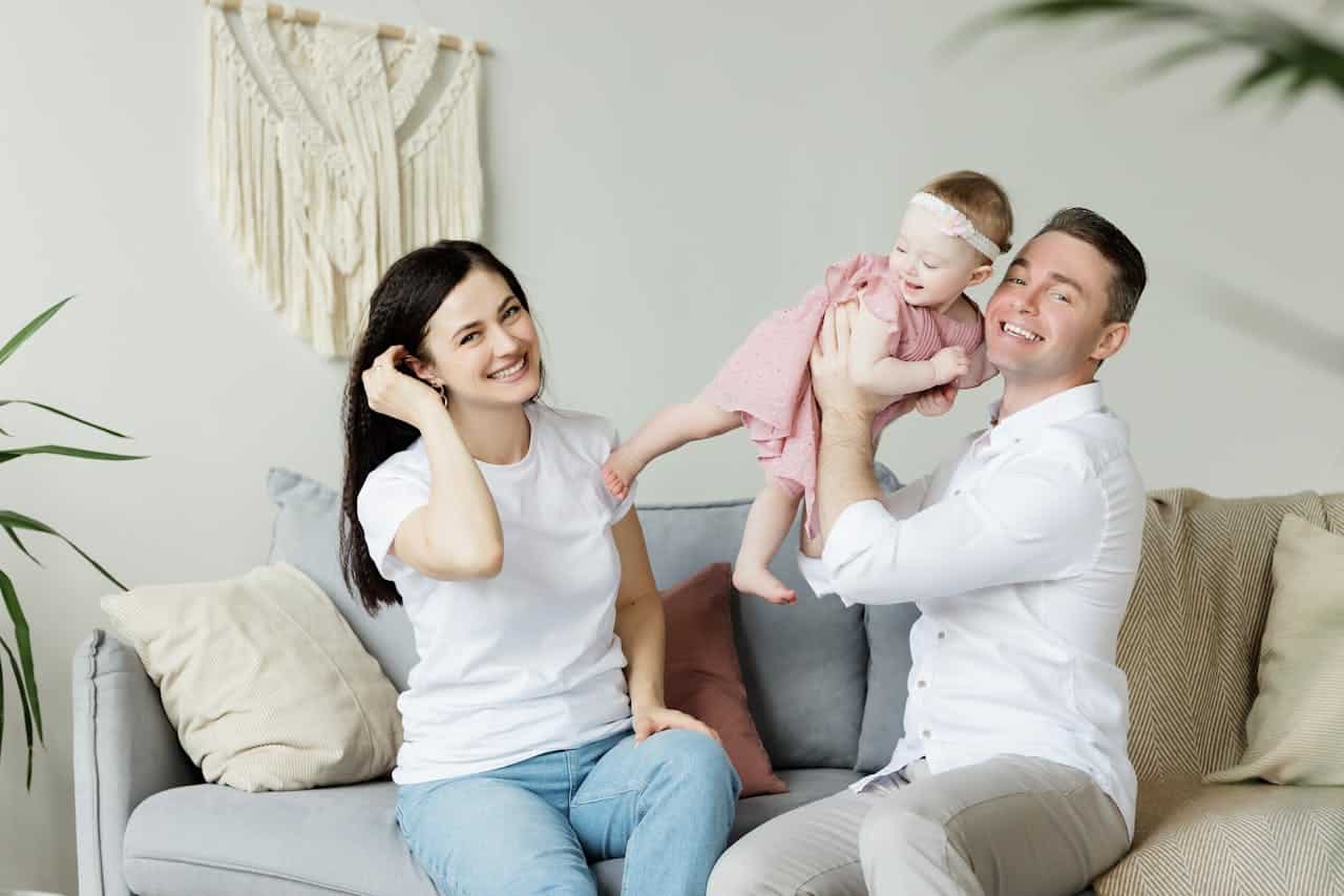Happy family in a cozy living room, parents playing with their baby, emphasizing the stability and joy of homeownership and family life.