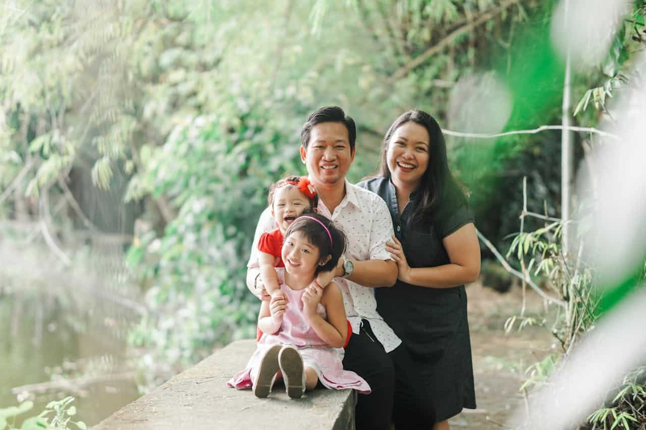 Family of four smiling together outdoors, representing stability and joy associated with homeownership and family life.