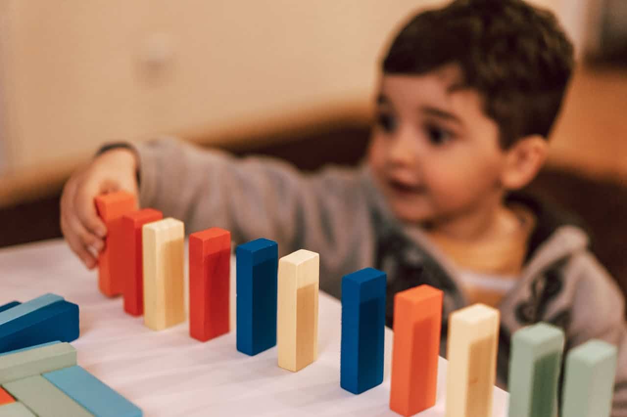 Child playing with colorful building blocks, focusing on arranging red, blue, yellow, and green pieces on a table, illustrating creativity and learning through play.