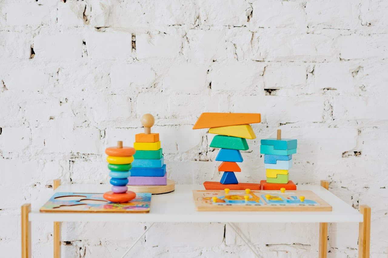 Colorful wooden stacking toys and puzzles on a white table against a brick wall, illustrating educational play for children.