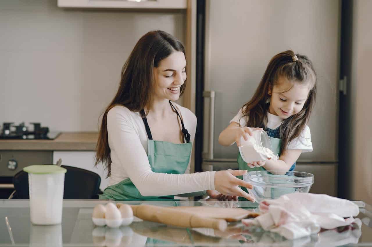 Mother and daughter baking together in a kitchen, measuring flour into a bowl, emphasizing family bonding and home cooking.