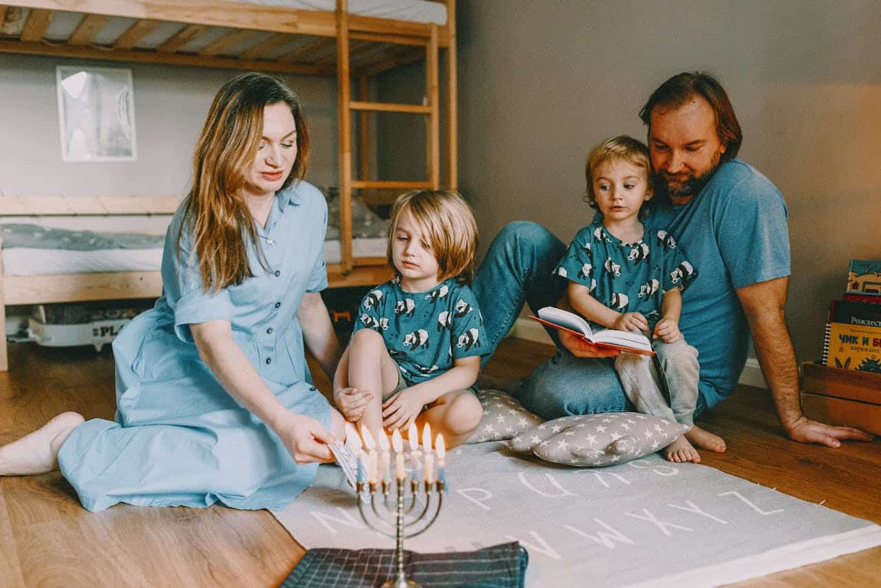 Family celebrating a holiday, lighting menorah candles, with children reading and engaging in a cozy home setting.