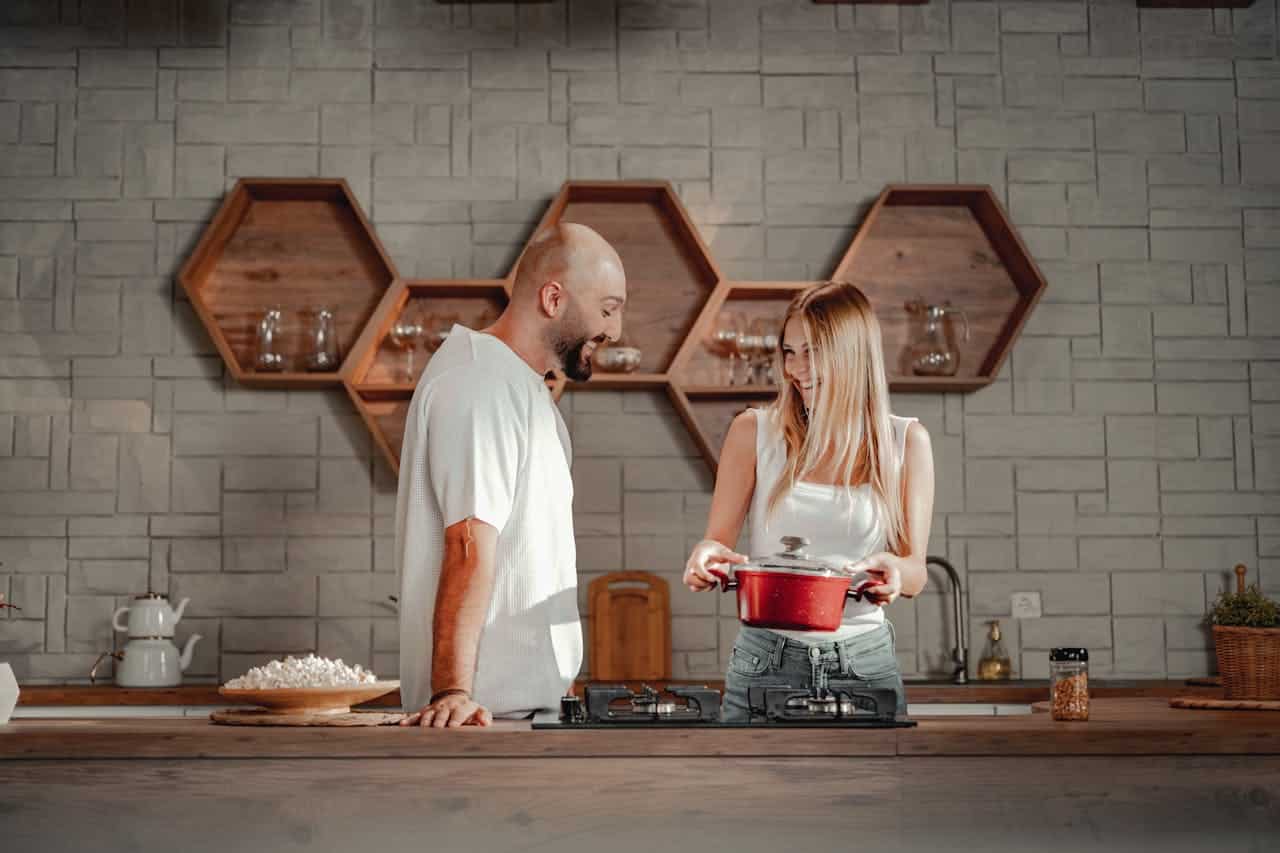 Couple in modern kitchen, smiling and interacting, woman holding a red pot, preparing food together.