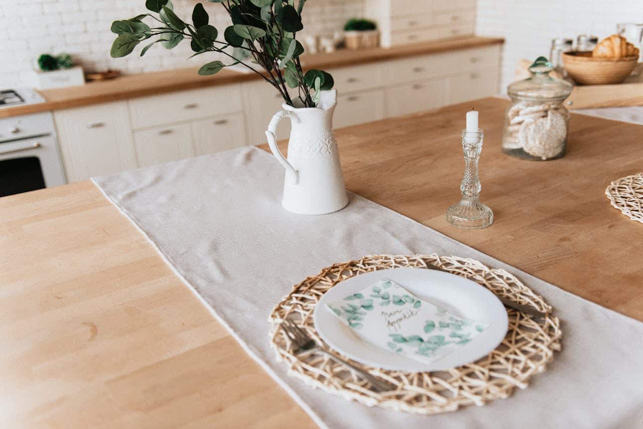 Table setting featuring a white pitcher with greenery, a decorative plate on a woven placemat, a candle holder, and a jar of cookies, representing a cozy home environment ideal for short-term ownership or transitional situations.