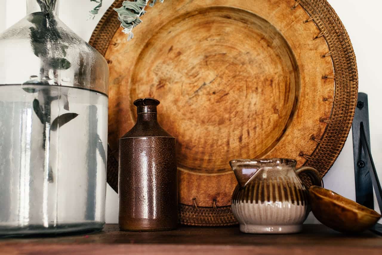 Decorative arrangement of a glass vase with foliage, a brown ceramic bottle, a striped pottery jug, and a wooden platter, emphasizing home decor elements relevant to owner financing themes.