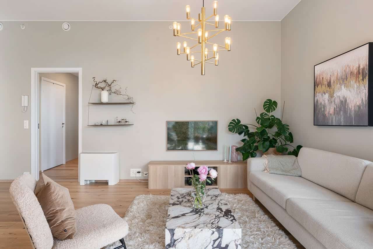 Modern living room with a stylish chandelier, plush sofa, marble coffee table, and decorative plants, reflecting a welcoming atmosphere for potential homeowners considering owner financing options.